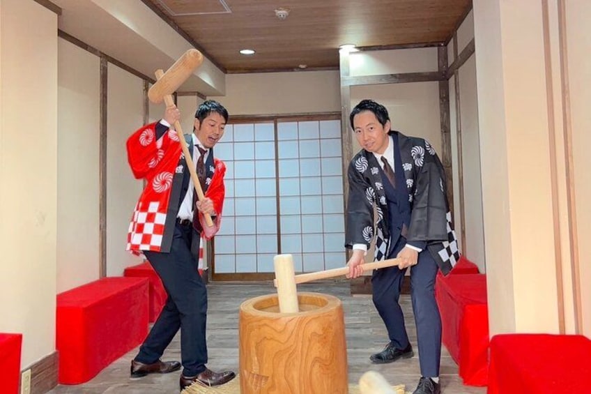 Two men in traditional attire playing a game with wooden mallets and a central wooden object. 2