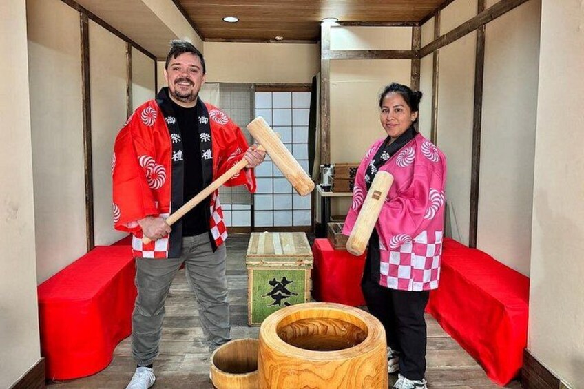 To personer i traditionelt japansk tøj holder træklubber, stående i et rum med tatamimåtter og en træfad. 3