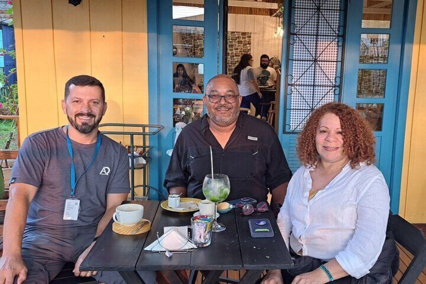 Three people seated at an outdoor table with drinks and a menu. 4