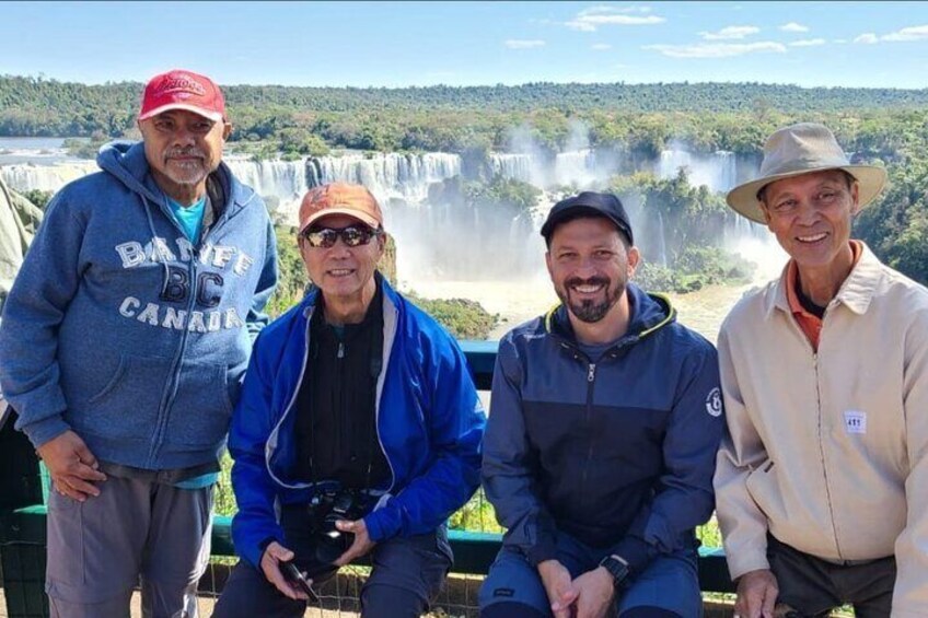 Four people standing in front of a waterfall with a forested landscape in the background. 1
