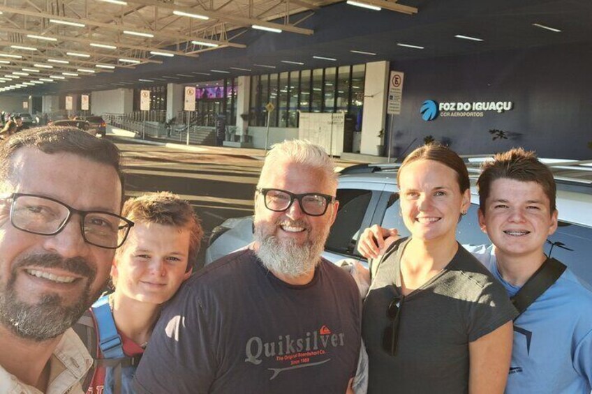 A group of people standing in front of an airport terminal with a sign that reads 'FOZ DO IGUÁU.' 3