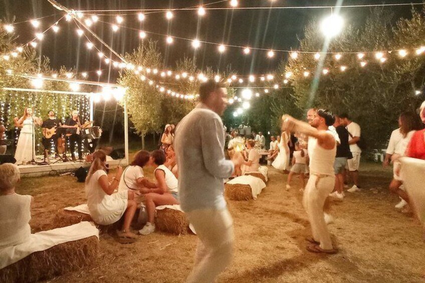 An outdoor event with string lights, a stage with a band, and people sitting on hay bales. 3
