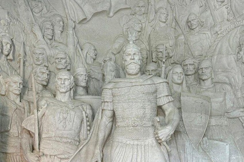 Eine detaillierte Steinhöhelniskulptur, die eine historische Schlacht mit Soldaten und einer zentralen Figur in Rüstung zeigt. 4