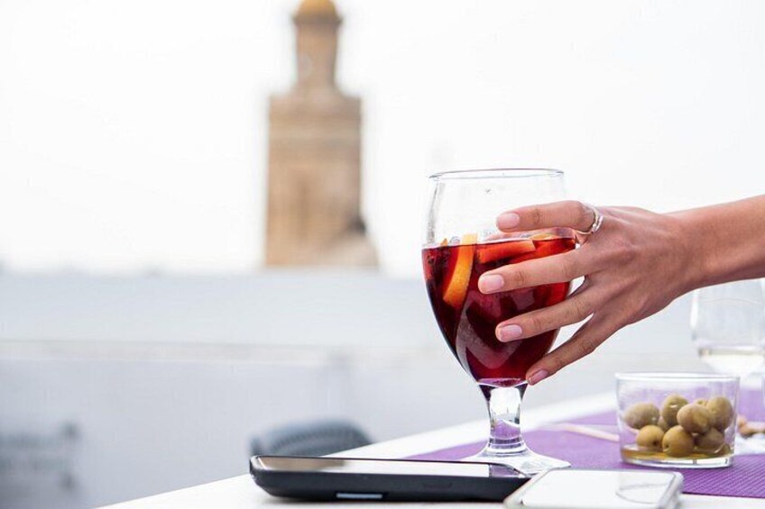 Una mano sosteniendo una copa de vino con líquido rojo y una rodaja de naranja. 3