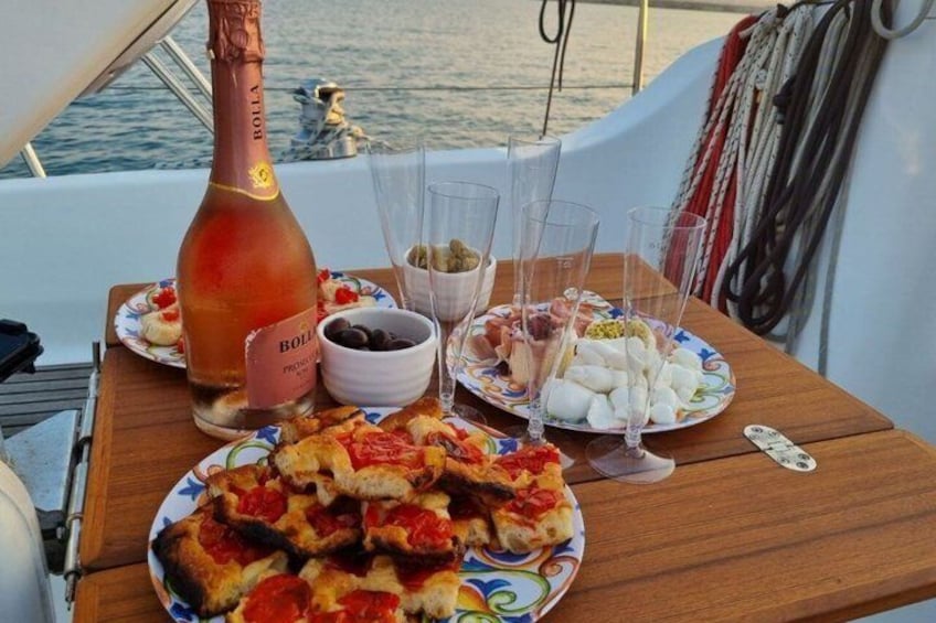 Een tafel op een boot, met een fles Bolla champagne, borden eten en glazen. 2
