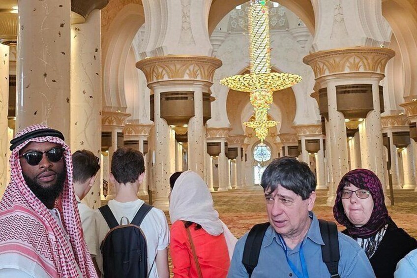 Un groupe de personnes se trouve à l’intérieur d’un bâtiment imposant, orné de colonnes richement décorées et surmonté d’un grand lustre. 5