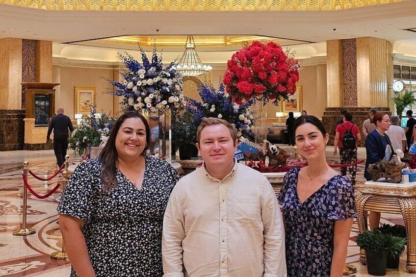 Trois personnes se tiennent dans un hall d’entrée décoré, agrémenté de compositions florales et d’un lustre. 4
