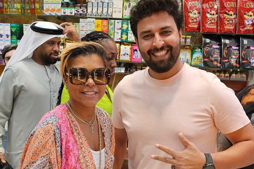 A person in a light pink shirt and sunglasses, another in a patterned shawl, and a third in traditional attire, standing in a store with shelves of packaged goods. 2