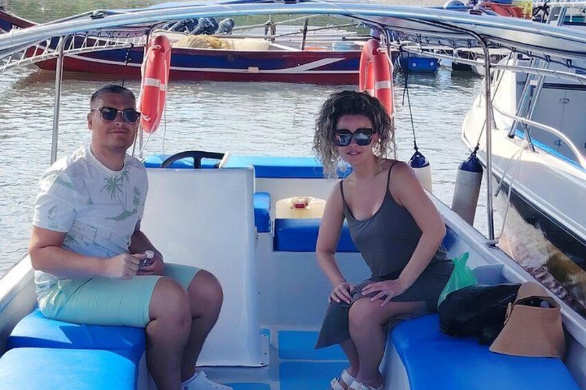 Two people sitting on a boat with blue cushions, a steering wheel, and life jackets. 3