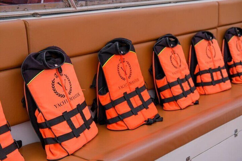A row of orange life jackets with black straps and the text "YACHT MASTER" on a brown bench. 2