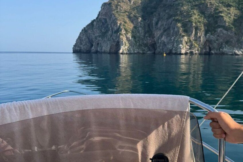 A boat with a person holding the railing, calm water, and a rocky island in the background. 2