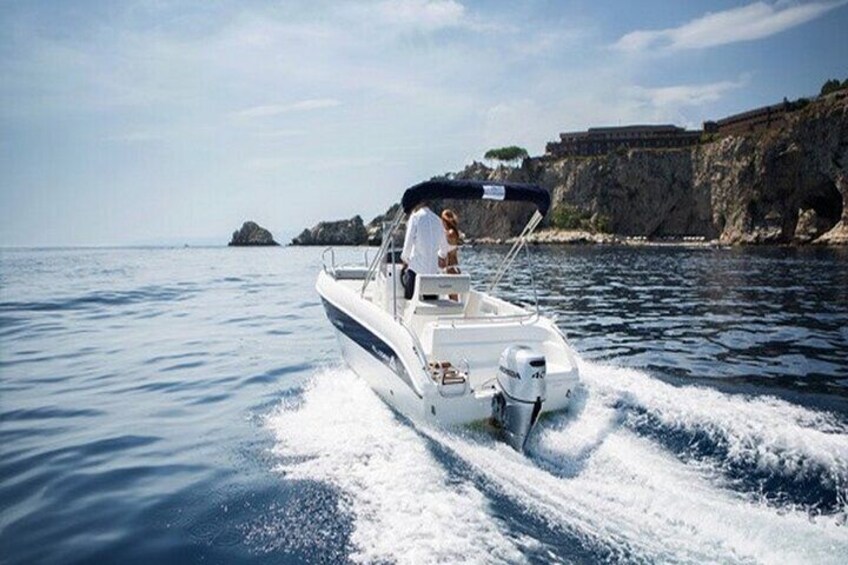 A white motorboat with a person steering, moving through calm waters near rocky cliffs. 1