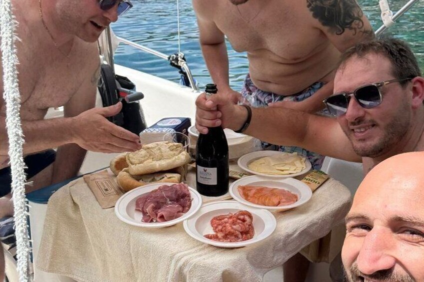 A group of people on a boat with a table set with food and a bottle of wine. 3