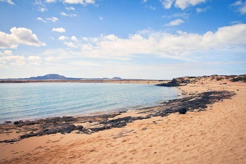 Una playa con agua cristalina, orilla arenosa y montañas a lo lejos. 5