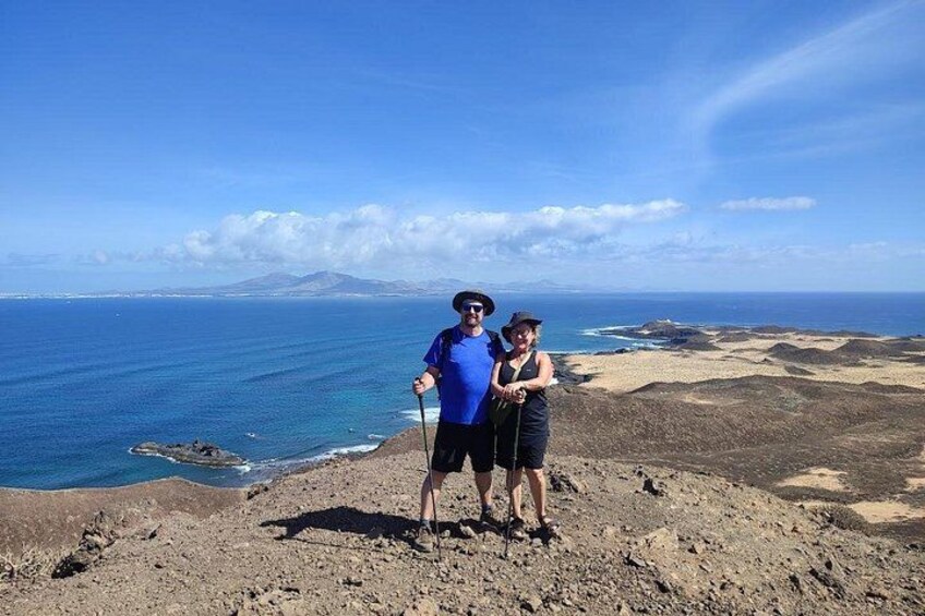 Dos personas en terreno rocoso, con vista al océano y montañas distantes. 2