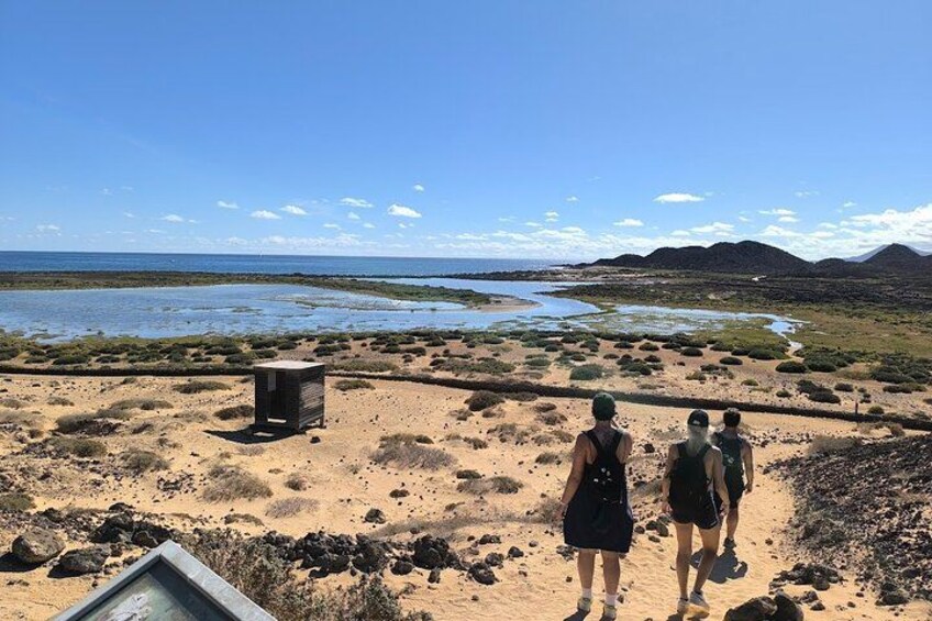 Paisaje desértico con una estructura pequeña, una masa de agua y montañas al fondo. 1