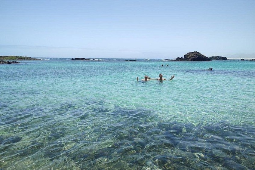 Mar azul cristalina con gente nadando y una isla rocosa a lo lejos. 2