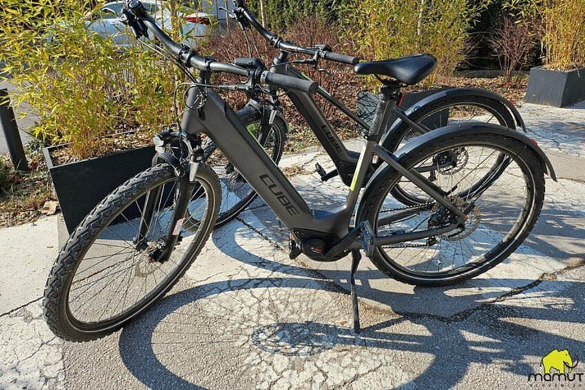 En svart elcykel står parkerad på en betongyta, och en korg är fastsatt framtill. 3