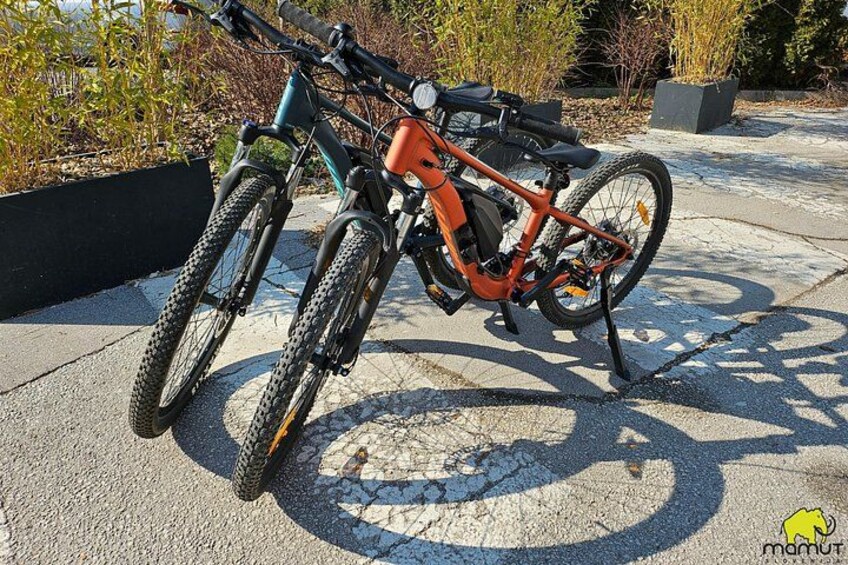 En mountainbike parkerad på en betongyta, bredvid ett cykelställ. 2