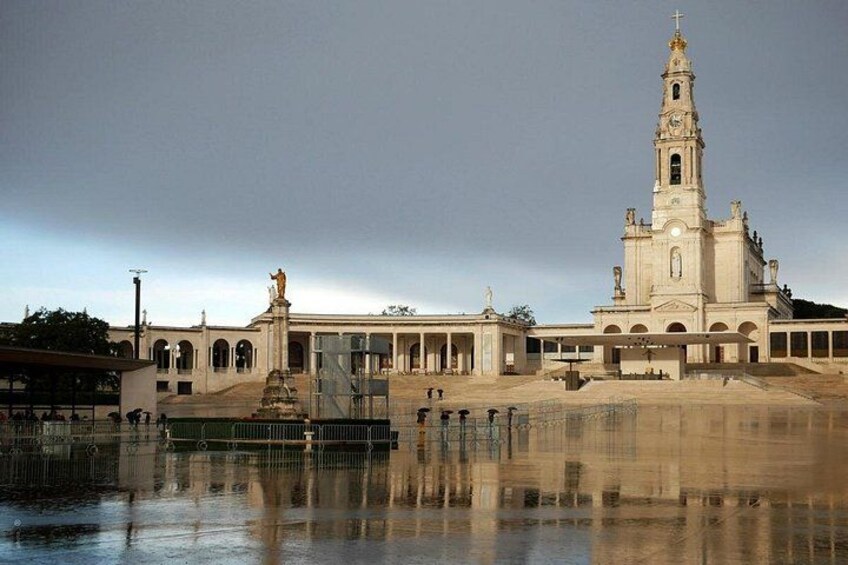 A large church with a bell tower, a fountain, and a reflection in the water. 3