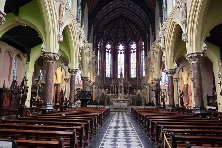 Interno di una chiesa con file di bancali, vetrate colorate e un'alta volta a botte. 4