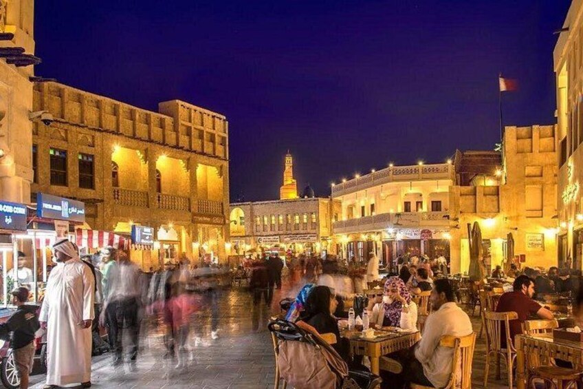 A bustling square with people walking and dining, historic buildings, and a prominent tower in the background. 2