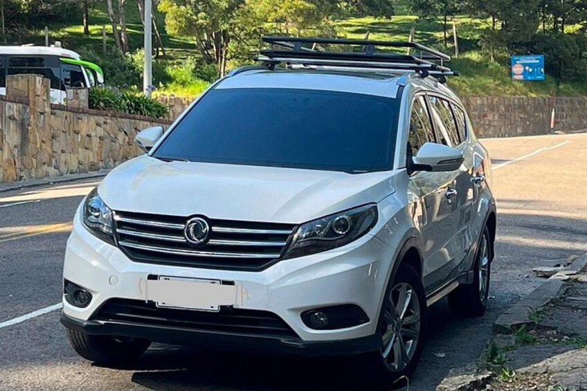 A white SUV parked on a road with a stone wall and greenery in the background. 2