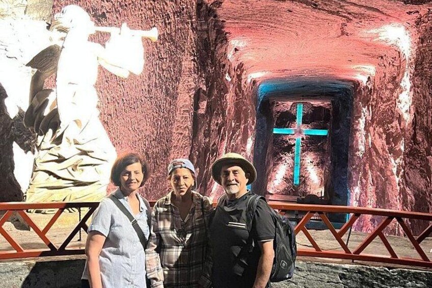 A cave entrance with a cross, a statue, and a metal railing. 4
