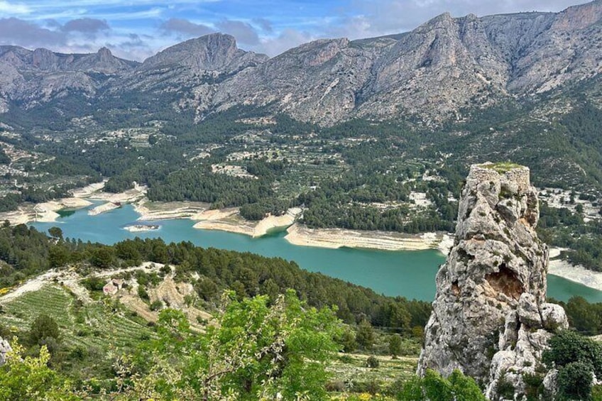 Eine Berglandschaft mit einer markanten Felsformation im Vordergrund und einem Tal mit mehreren Seen im Hintergrund. 1