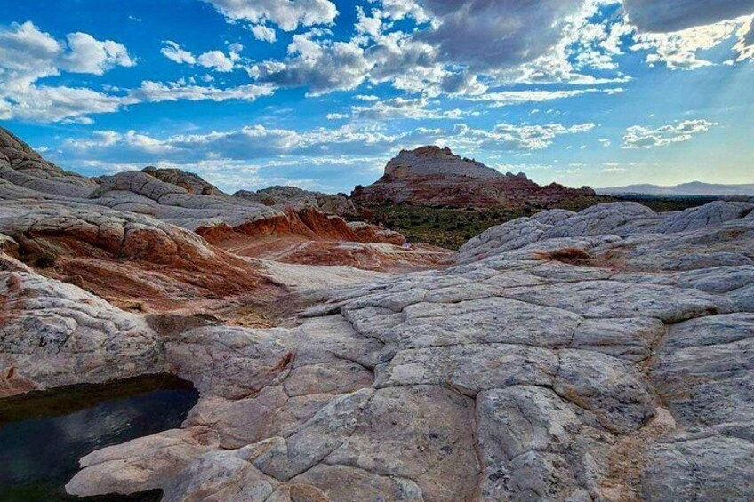 A rocky landscape with layered sedimentary rock formations and a small water body. 4