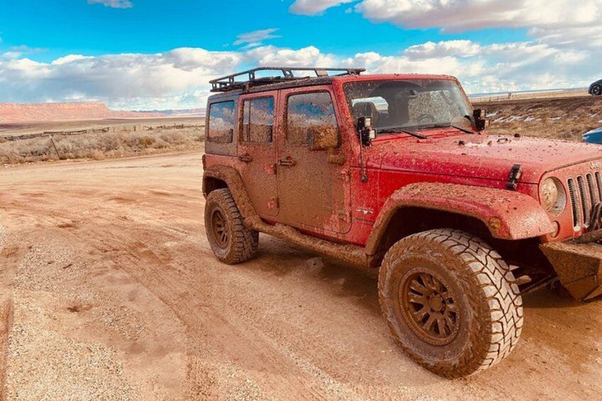 A red off-road vehicle parked on a dirt road in a desert landscape. 3