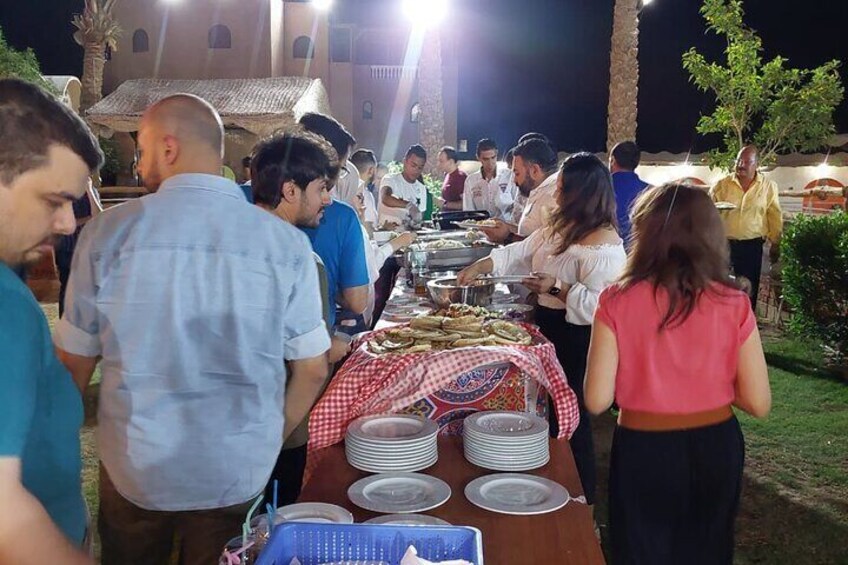 A group of people dining outdoors at night with a long table set with plates and food. 2
