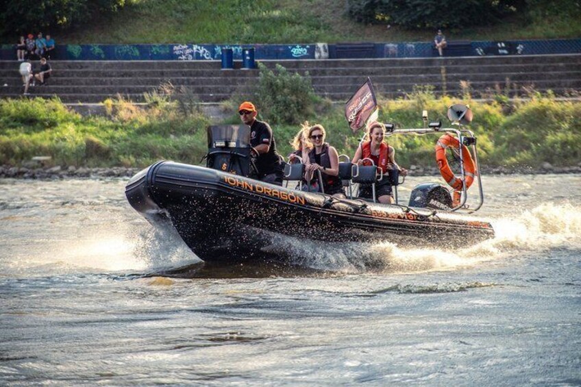 A speedboat with 'JOHN DRASSON' written on it, moving swiftly through water, with passengers and a flag. 5