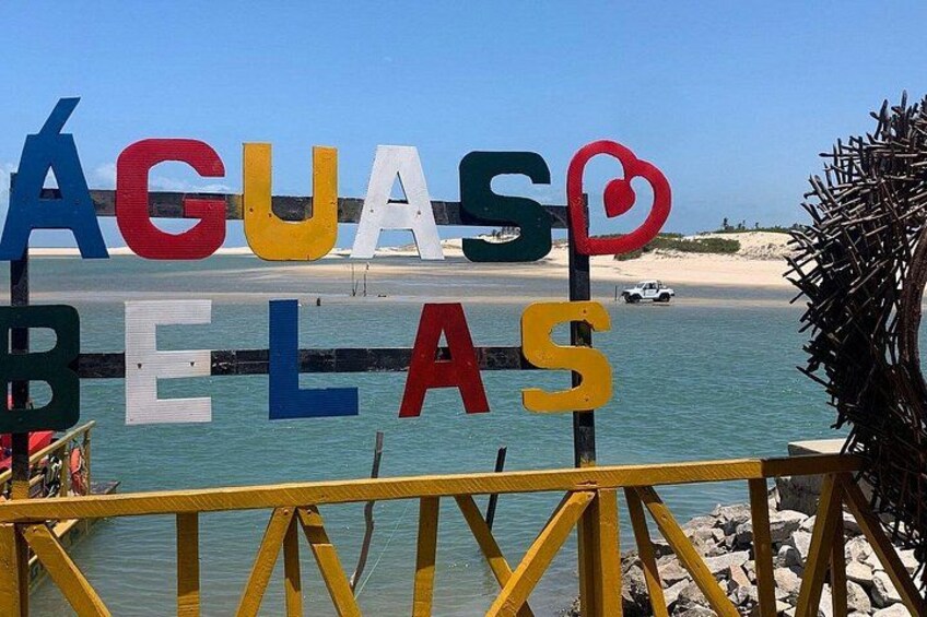 A beach with a sign reading 'ÁGUA BELAS' and a wooden railing in the foreground. 2