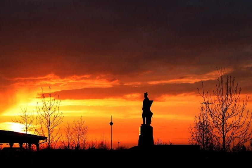 Silueta de una estatua contra un cielo al atardecer, con un banco y árboles desnudos en primer plano. 5