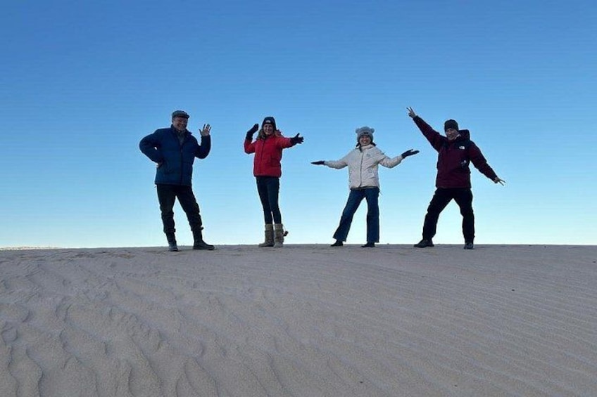 Four people standing on a sandy surface with a clear sky in the background. 1