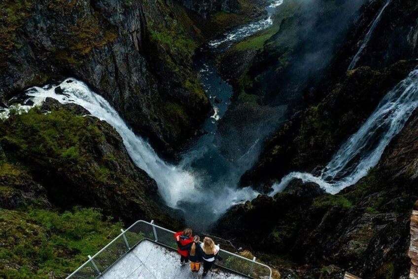 A waterfall cascading down a rocky gorge with a viewing platform and people observing. 2