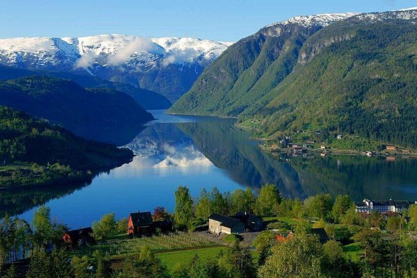 A lake surrounded by mountains with snow-capped peaks, a clear reflection, and a small settlement with houses and trees. 3