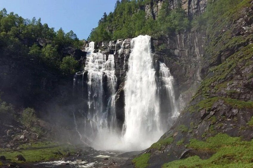 A multi-tiered waterfall cascading down a rocky cliff surrounded by lush greenery. 4