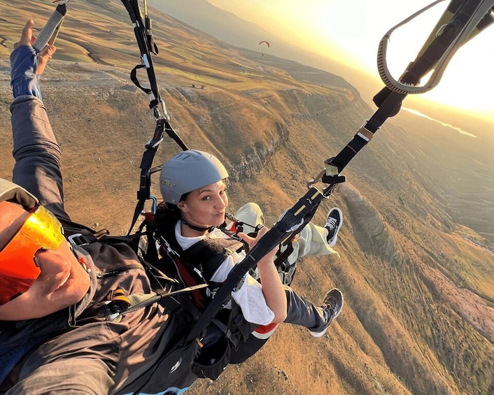A person paragliding with a harness and helmet, over a mountainous landscape during sunset. 1