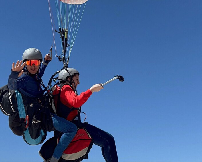 Two people paragliding with a clear blue sky in the background. 2
