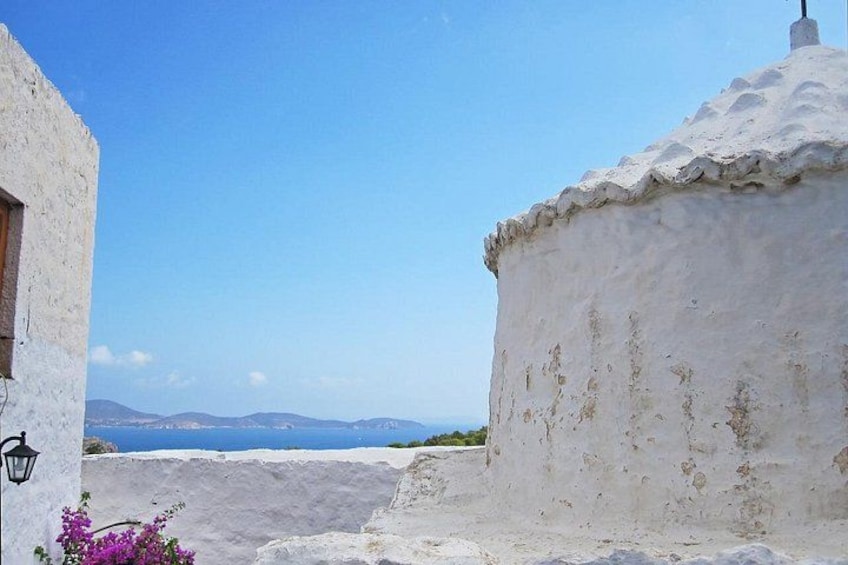 A coastal building with a white exterior, a clear blue sky, and a view of the sea and distant mountains. 5