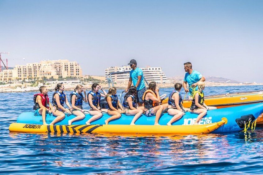 Un gruppo di persone su una barca gonfiabile gialla e blu sull'acqua, con edifici sullo sfondo. 3