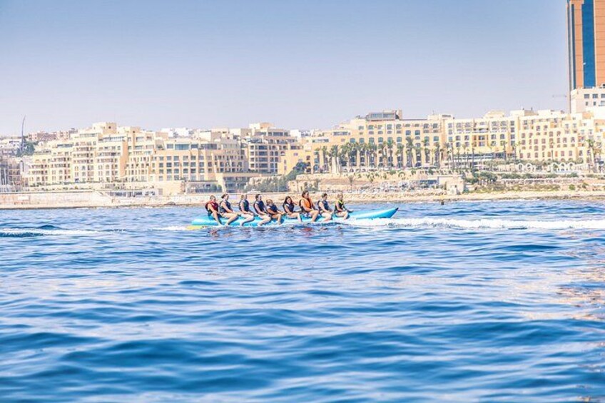 Una squadra di canottaggio su una barca in uno specchio d'acqua, con uno skyline urbano sullo sfondo. 2