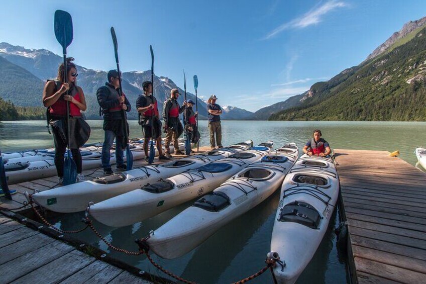People standing on a dock with kayaks and paddles. 1