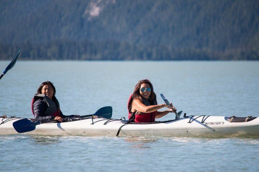 Two people kayaking on a calm lake with a forested shoreline in the background. 5