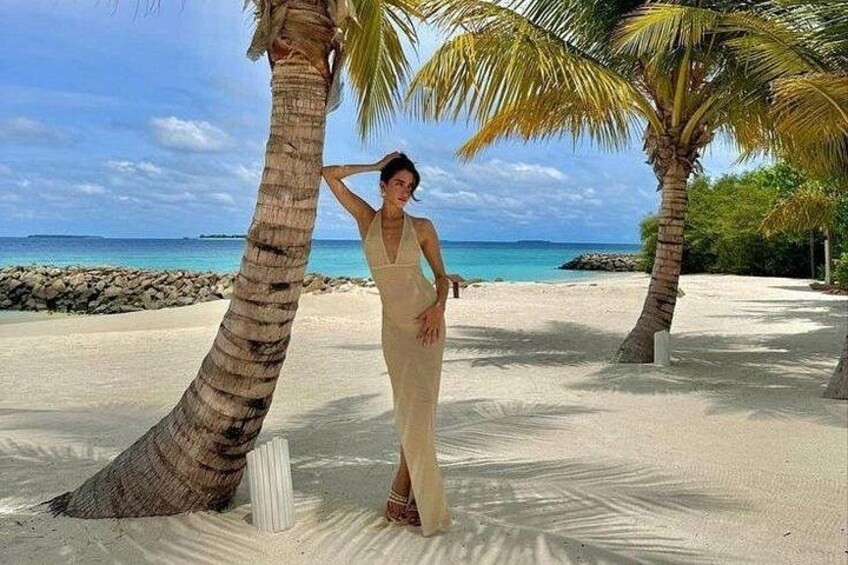 Una persona vestida parada en una playa arenosa con palmeras y un cielo azul despejado. 2