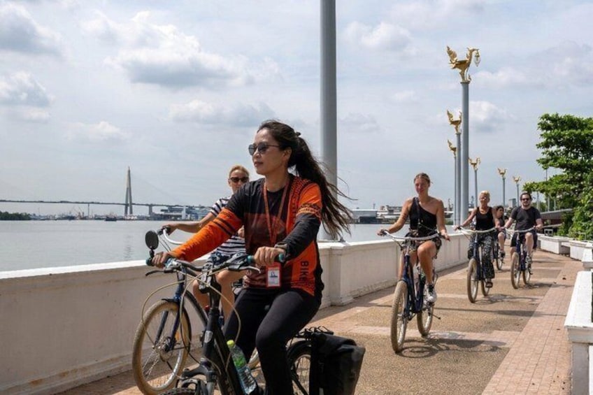Cyclists on a waterfront path with a bridge in the background. 1