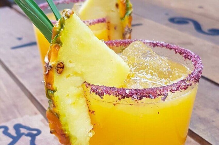 A glass of yellow drink garnished with a slice of pineapple and a sprig of green herb. 4