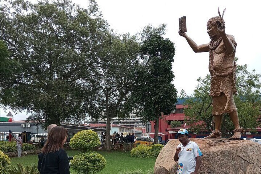 A statue of a person taking a selfie, a large rock, and a person standing in front of the statue. 1